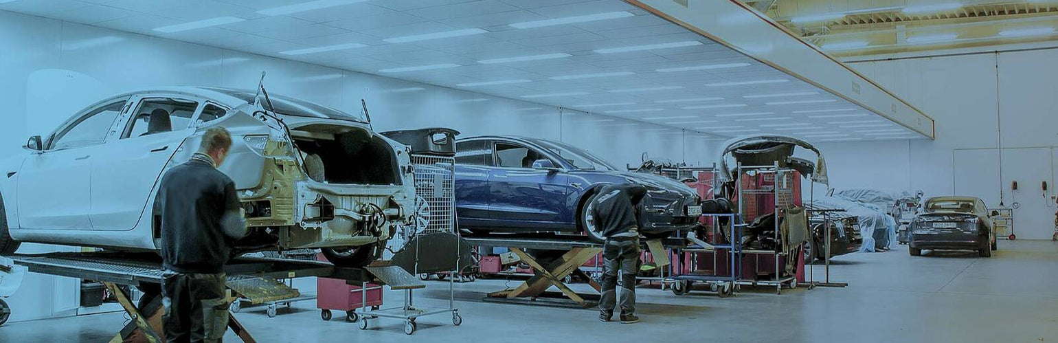 Technician working on Tesla battery components with tools and replacement parts.