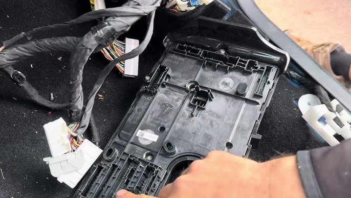 Technician working on Tesla battery components with tools and replacement parts.